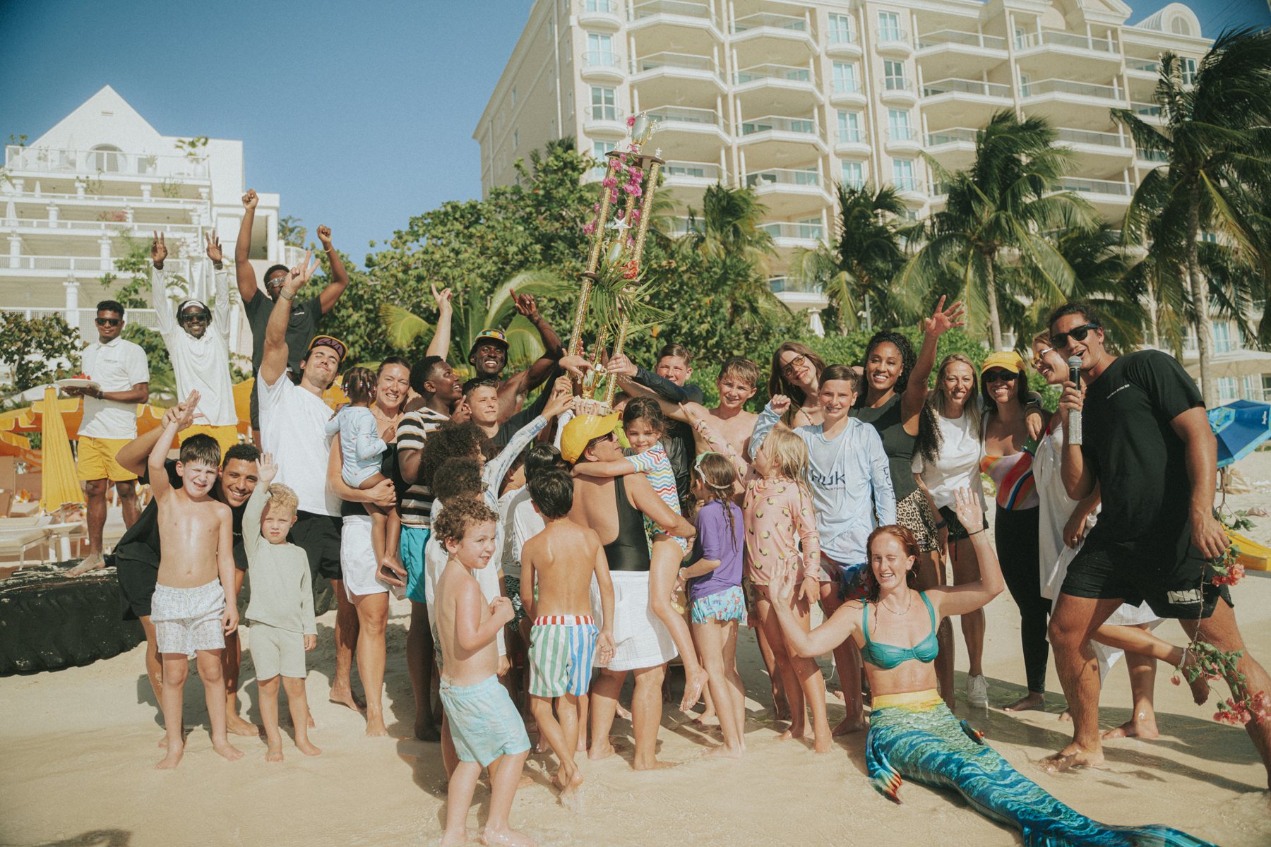 Families, children, coaches and hotel staff lifting the flower-dressed trophy at the Athlete Beach Challenge