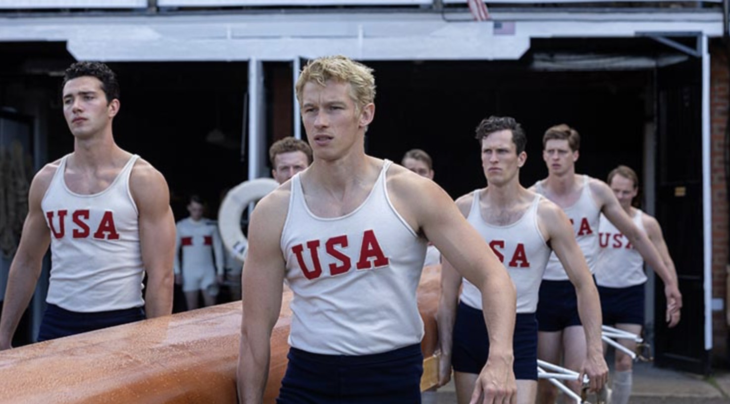 The crew carrying a wooden eight out of the boathouse in USA Olympic kit