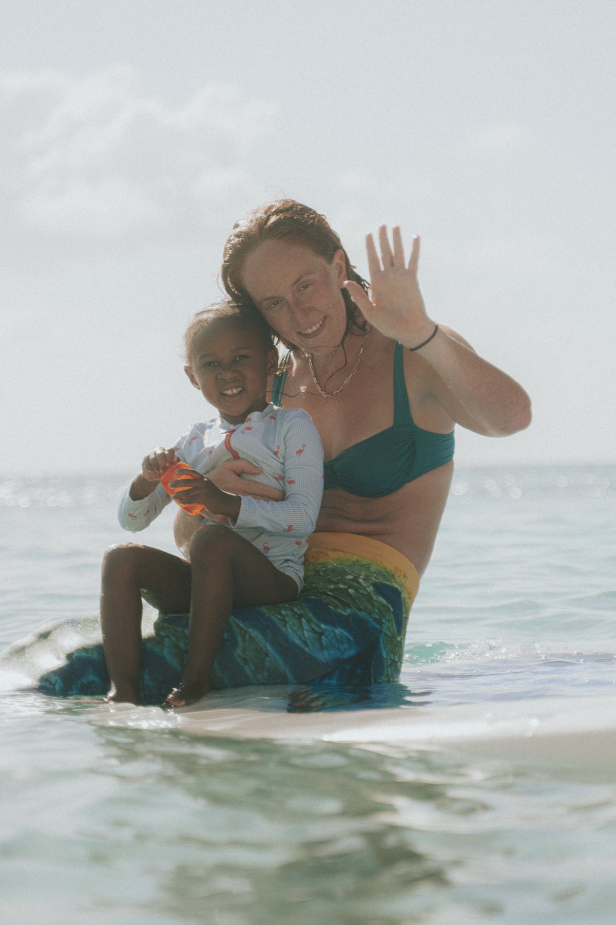 Olympic synchronised swimmer Eva Morris in a mermaid tail, waving from the shallows with a young guest on her lap