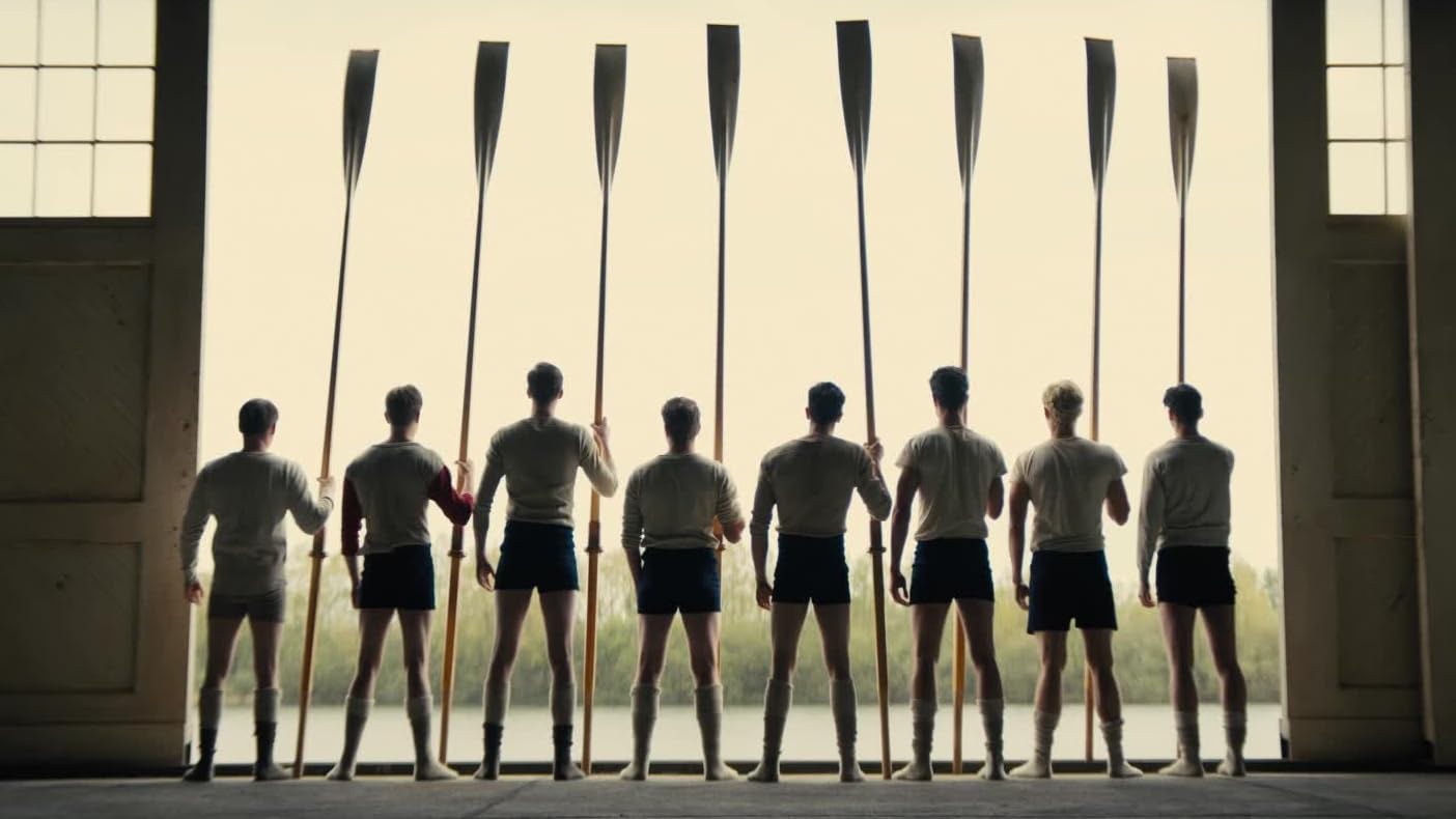 The crew with their oars in the boathouse doorway, looking out over the water