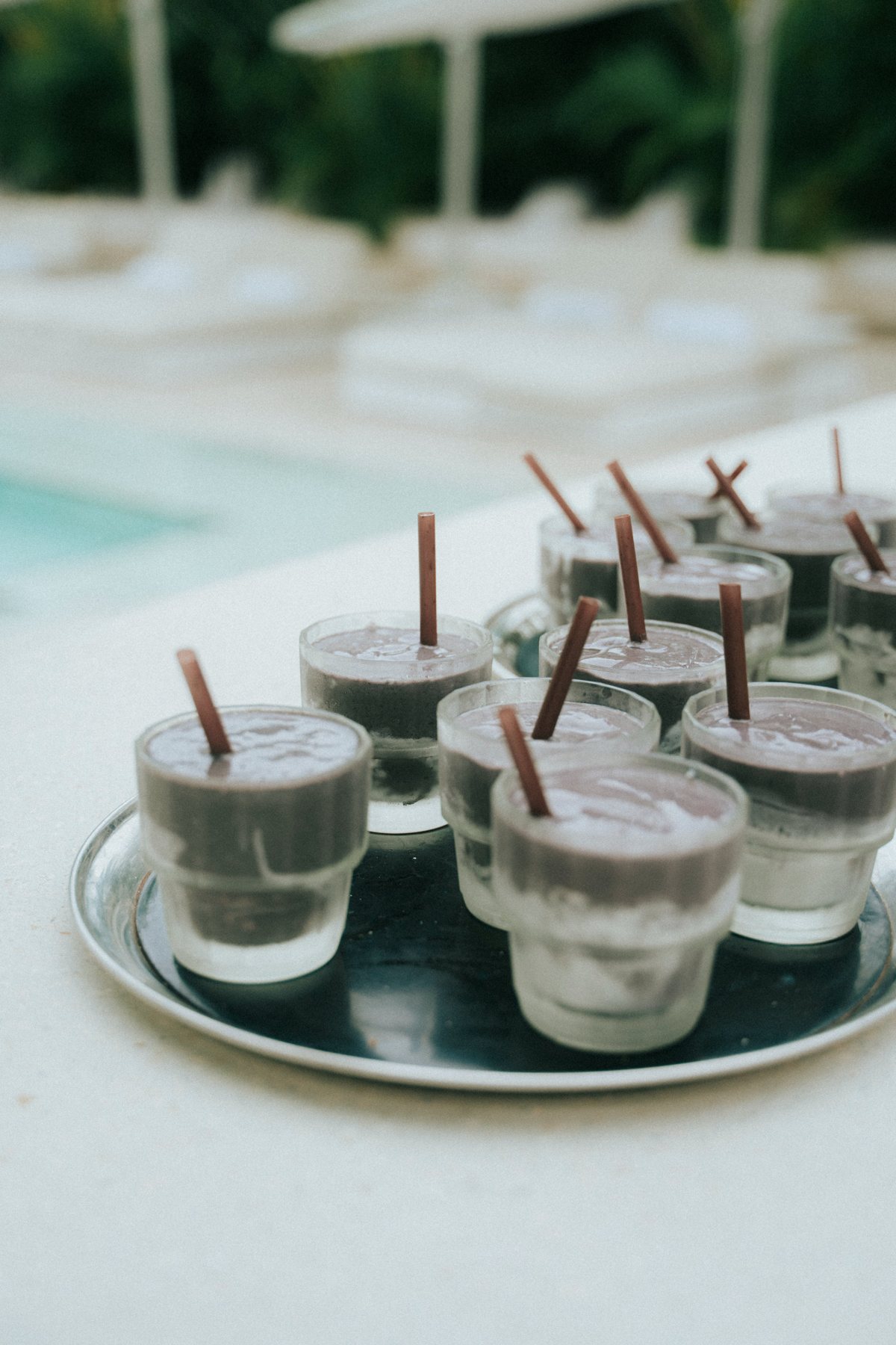 A silver tray of chocolate recovery smoothies in frosted glasses beside the pool