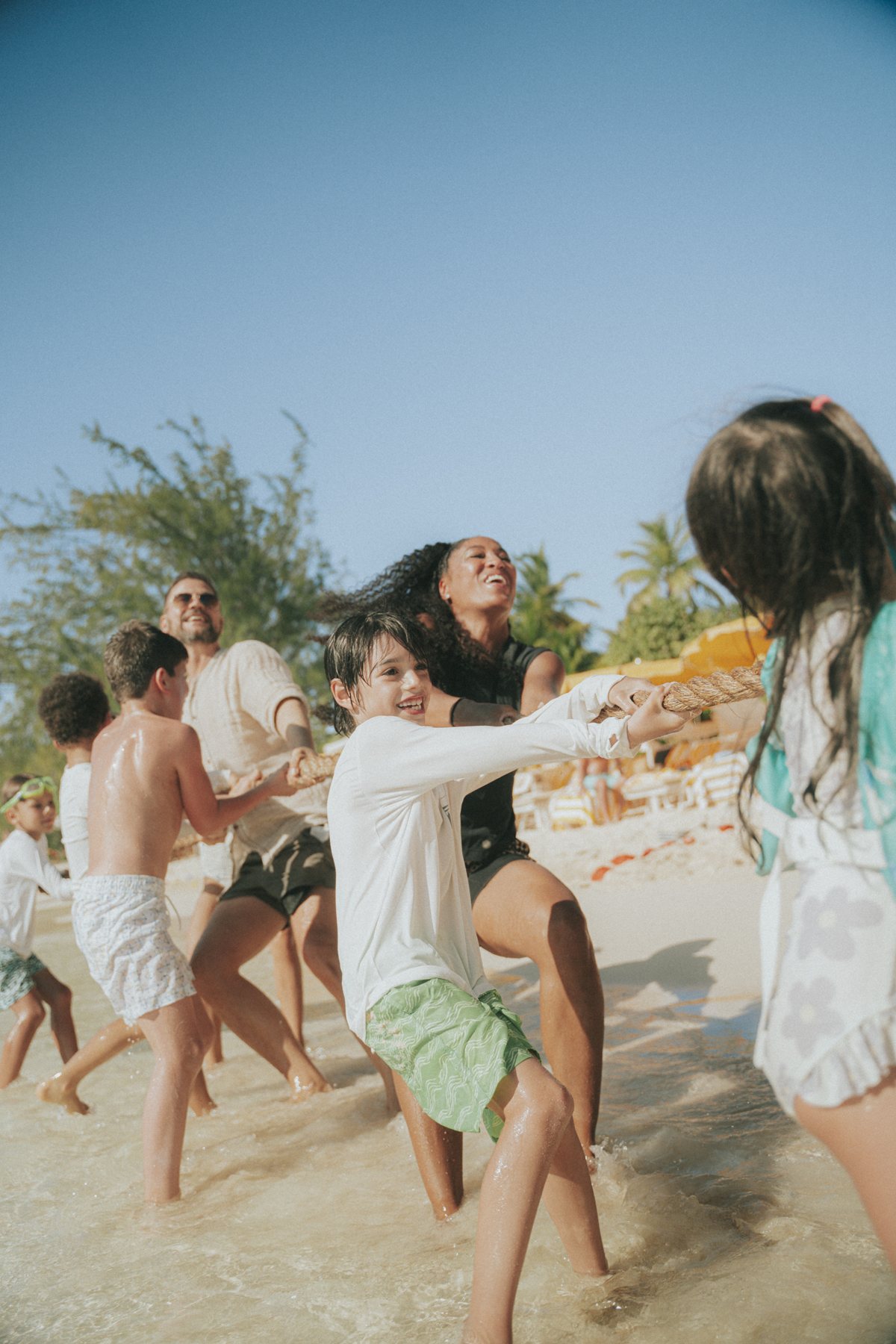 Children and adults laughing through a tug of war in the shallows